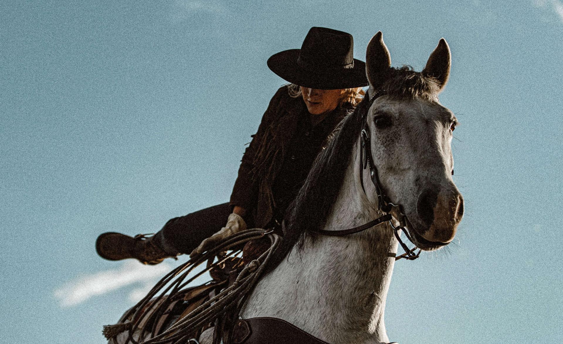 a woman in a cowboy hat mounting a white horse